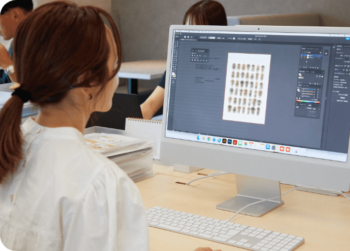 白いブラウスを着た人物がデスクトップPCでデザイン作業をしている